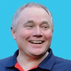 Smiling middle-aged man with short gray hair wearing a navy polo on a bright blue background.