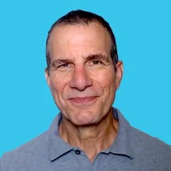 Portrait of a smiling middle-aged man wearing a light blue polo shirt against a blue background.