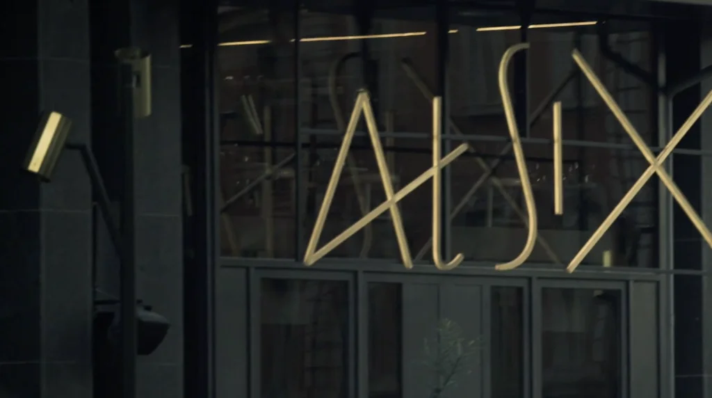 Storefront glass window with a large, geometric illuminated sign spelling 'ALEX' across it
